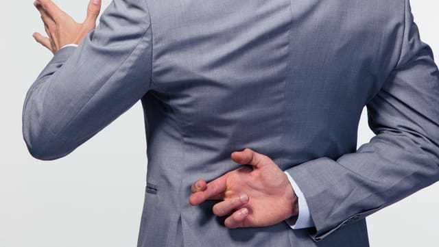 Ein Mann in Anzug spricht und überkreuzt hinter seinem Rücken die Finger. Ein Mann in Anzug spricht und überkreuzt hinter seinem Rücken die Finger.