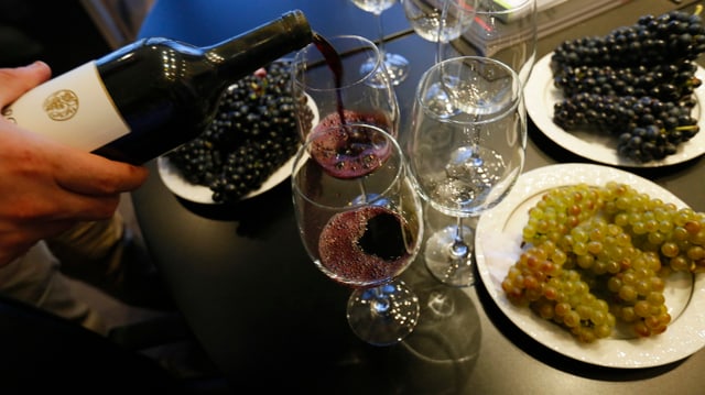 Eine Person schenkt in ein Glas Rotwein ein. Eine Person schenkt in ein Glas Rotwein ein.