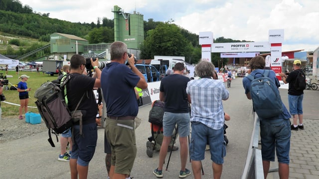 Fotografen stehen hinter dem Ziel, im Hintergrund eine Fahrerin mit erhobenen Händen auf dem Bike Fotografen stehen hinter dem Ziel, im Hintergrund eine Fahrerin mit erhobenen Händen auf dem Bike