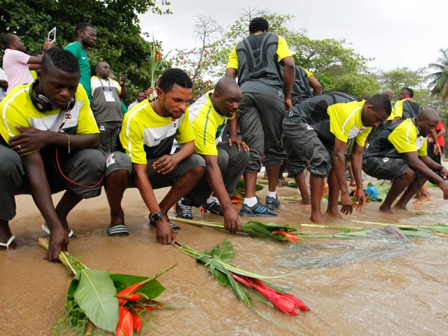 Männer in Sambia legen Blumen am Strand nieder.