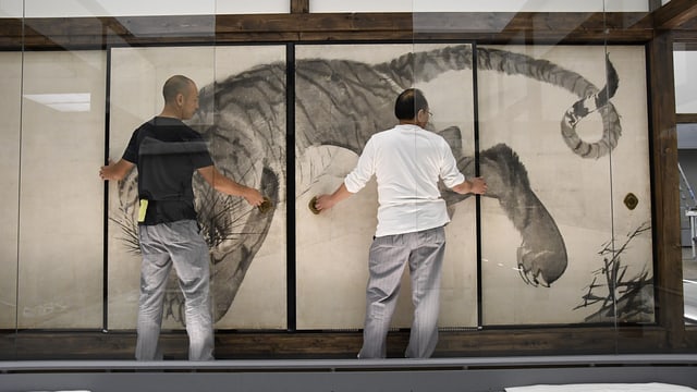 Zwei Männer stellen Bild an die Wand Zwei Männer stellen Bild an die Wand