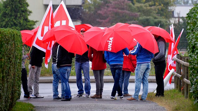 Eine Gruppe Unia-Vertreter steht unter Regenschirmen im Kreis.