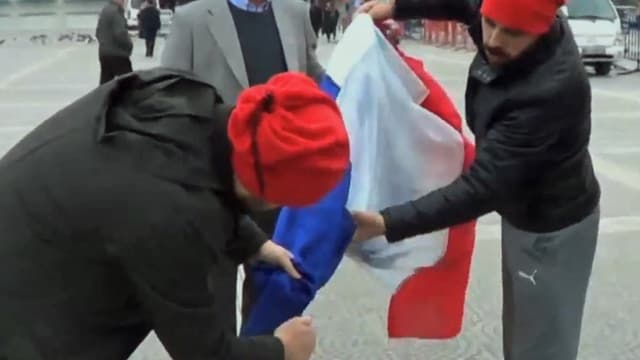 Zwei Männer zünden eine französische Flagge an.