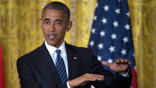 Obama vor einem goldenen Vorhang und US-Flagge mit bestimmtem Blick und gestikulierenden Händen. Obama vor einem goldenen Vorhang und US-Flagge mit bestimmtem Blick und gestikulierenden Händen.