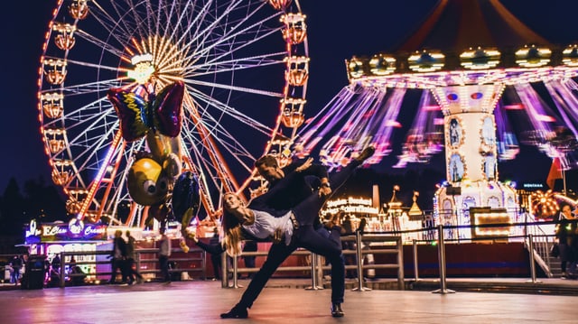 Ein Tänzer und eine Tänzerin nachts vor einem Riesenrad. Ein Tänzer und eine Tänzerin nachts vor einem Riesenrad.
