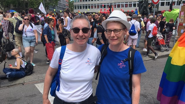 Zwei Frauen. Im Hintergrund Menschen und bunte Fahnen sowie Ballone. Zwei Frauen. Im Hintergrund Menschen und bunte Fahnen sowie Ballone.