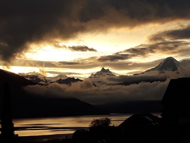 Morgenstimmung mit Blick auf See, Berge im Hintergrund und Wolken am Himmel.