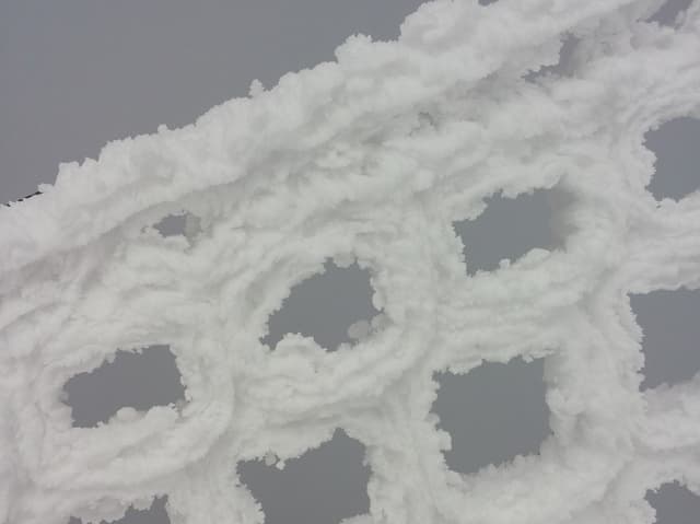 Die Maschen eines Absperrnetzes sind von Schnee überdeckt. Mit den Löchern dazwischen sieht es aus wie gespritzter Rahm.