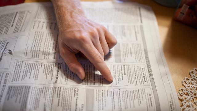 Arbeitsloser Mann sucht in Aargauer Zeitungsteil nach Stellen (zu sehen ist seine Hand). Arbeitsloser Mann sucht in Aargauer Zeitungsteil nach Stellen (zu sehen ist seine Hand).