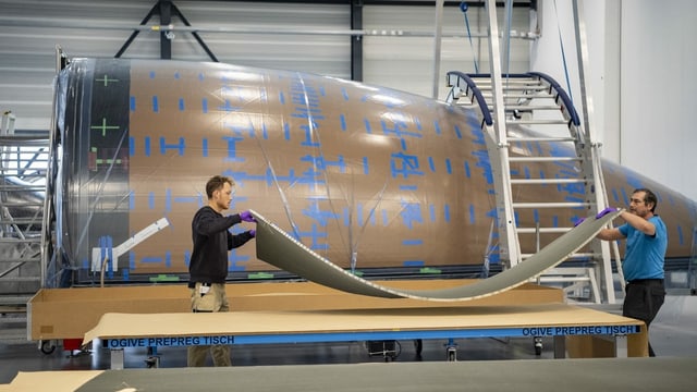 Mitarbeiter bereiten eine der Materialschichten vor. Im Hintergrund die bereits belegte Backform der Raketenspitze. Mitarbeiter bereiten eine der Materialschichten vor. Im Hintergrund die bereits belegte Backform der Raketenspitze.