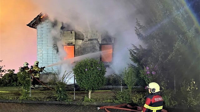 Brennendes, älteres Einfamilienhaus, im Vordergrund Feuerwehrmann Brennendes, älteres Einfamilienhaus, im Vordergrund Feuerwehrmann