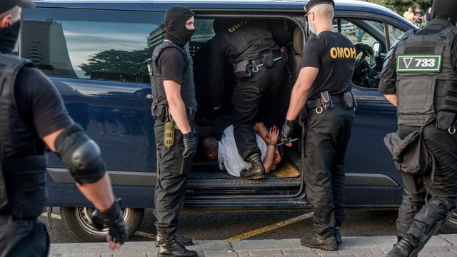 Vermummten Polizisten stecken Mann in Polizeiwagen. Vermummten Polizisten stecken Mann in Polizeiwagen.