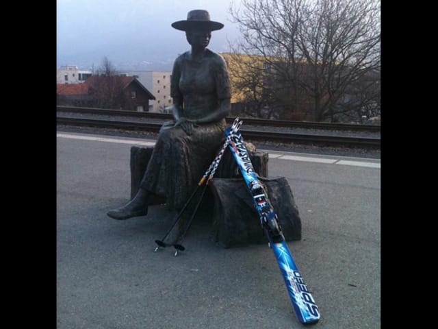 Statue einer sitzenden Frau, an die Ski gelehnt sind.