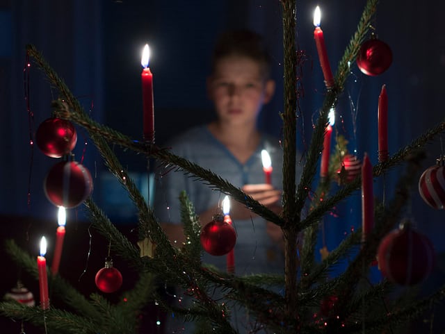 Knabe durch einen klassischen Weihnachtsbaum mit brennenden roten Kerzen und roten Kugeln fotografiert