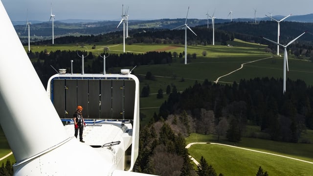 Ein Mann steht auf einer Windturbine, im HIntergrund weitere Turbinen. Ein Mann steht auf einer Windturbine, im HIntergrund weitere Turbinen.