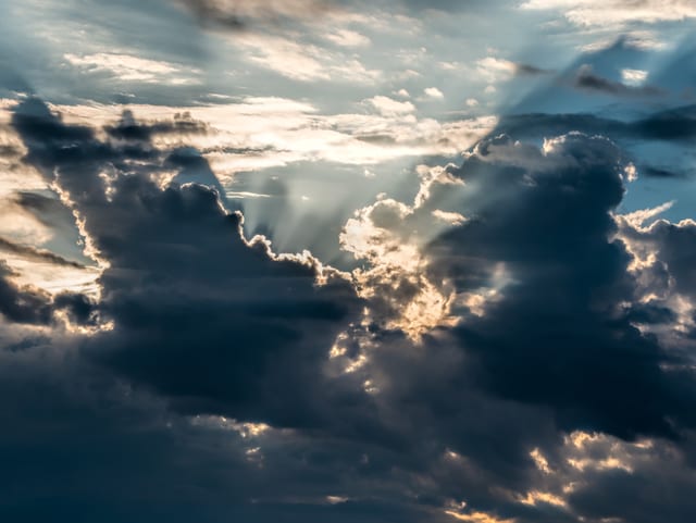 Bewölkter Himmel mit dunklen Wolkentürmen und einigen Sonnenstrahlen dahinter.