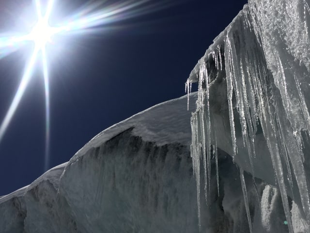 Blauer Himmel, Sonne links oben, rechts unten Eiszapfen mit Eisschild.