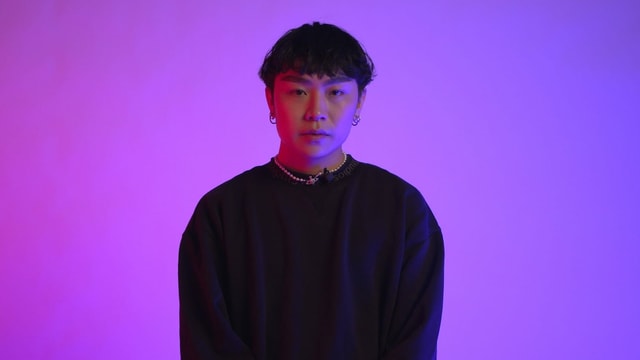 Brian hat schwarze Haare und trägt einen schwarzen Pulli und eine Goldkette. Brian hat schwarze Haare und trägt einen schwarzen Pulli und eine Goldkette.