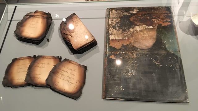 Verkohlte Dokumente und ein schwer beschädigtes Gemälde. Verkohlte Dokumente und ein schwer beschädigtes Gemälde.