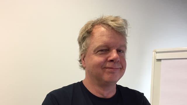 Ein Mann mit blonden Haaren steht vor einer weissen Wand und blickt in die Kamera. Ein Mann mit blonden Haaren steht vor einer weissen Wand und blickt in die Kamera.