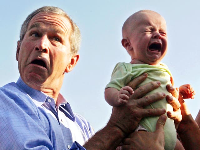 George W. Bush (links) ein weinendes Baby in den Händen haltend
