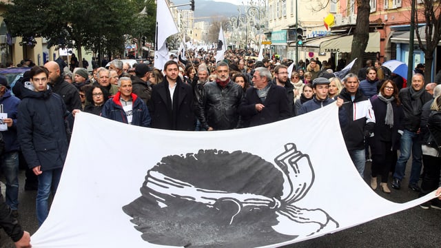 Demonstranten tragen riesiges Tuch mit Korsenkopf. Demonstranten tragen riesiges Tuch mit Korsenkopf.