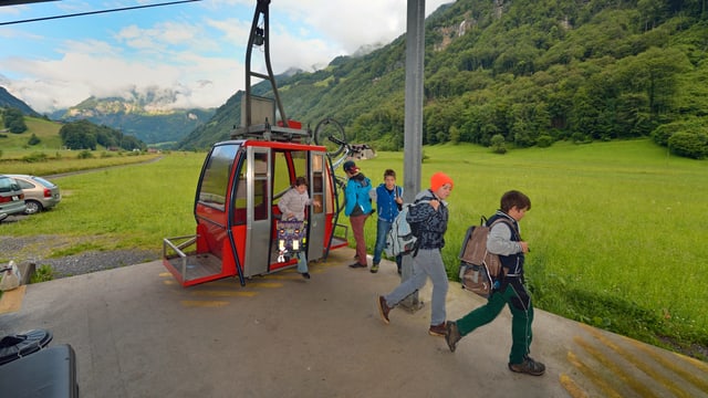 Schülerinnen und Schüler steigen aus einer roten Seilbahnkabine aus. Schülerinnen und Schüler steigen aus einer roten Seilbahnkabine aus.