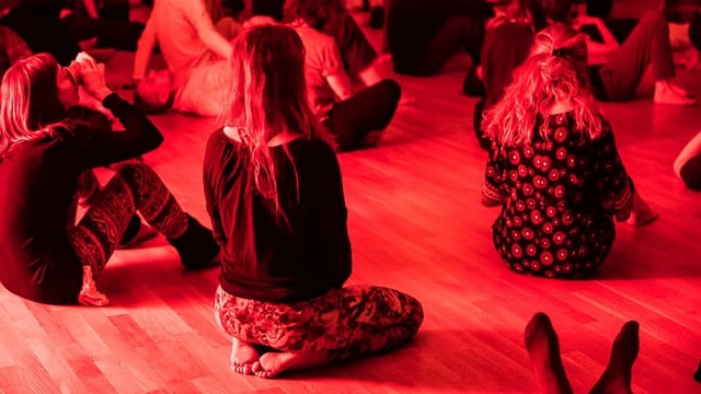 Menschen sitzen am Boden in einem rot beleuchteten Raum Menschen sitzen am Boden in einem rot beleuchteten Raum