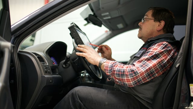 Garagist Schär sitzt im Auto und tippt auf ein Tablet-Computer. Garagist Schär sitzt im Auto und tippt auf ein Tablet-Computer.