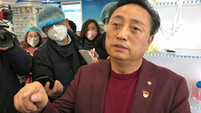 Direktor Wu ohne Gesichtsmaske, dahinter offensichtlich Journalisten, mit Gesichtsmasken. Direktor Wu ohne Gesichtsmaske, dahinter offensichtlich Journalisten, mit Gesichtsmasken.