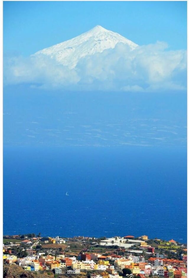 Unten im Bild eine farbige Küstenstadt der Insel Gran Canaria. Dahinter blaues Meer mit einem Segelschiff. Am Horizont ist Teneriffa und über den Wolken der weisse Gipfel des Pico del Teide zu sehen. Unten im Bild eine farbige Küstenstadt der Insel Gran Canaria. Dahinter blaues Meer mit einem Segelschiff. Am Horizont ist Teneriffa und über den Wolken der weisse Gipfel des Pico del Teide zu sehen.