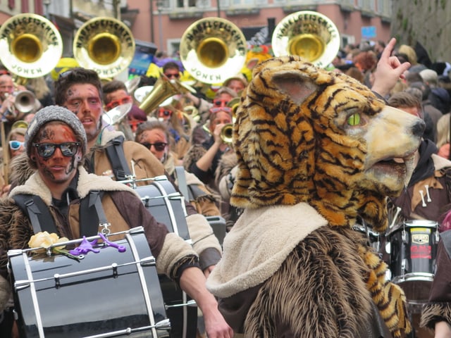 Tambourmajor mit Löwenkopf, dahinter Guggenmusik in Fellkleidern
