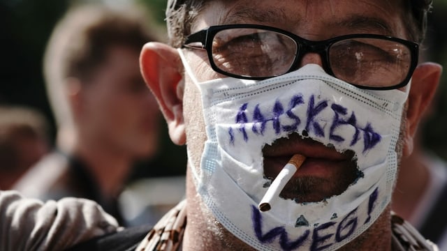 Ein Mann mit einer zerschnittenen Maske und einer Zigarette Ein Mann mit einer zerschnittenen Maske und einer Zigarette