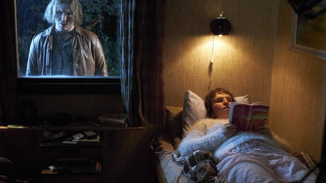 Ein unheimlich aussehender Mann steht draussen vor dem Fenster, währenddem sie im Bett liegt.