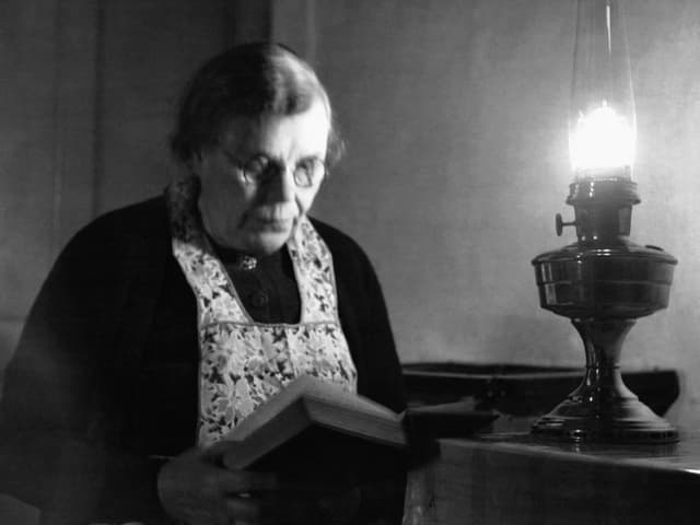 Eine Frau liest. Auf dem Tisch steht eine Kerosinlampe. Eine Frau liest. Auf dem Tisch steht eine Kerosinlampe.