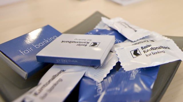 Eine Schale mit Zündholzschachteln und Bonbonverpackungen, die das BKB-Logo tragen. Eine Schale mit Zündholzschachteln und Bonbonverpackungen, die das BKB-Logo tragen.