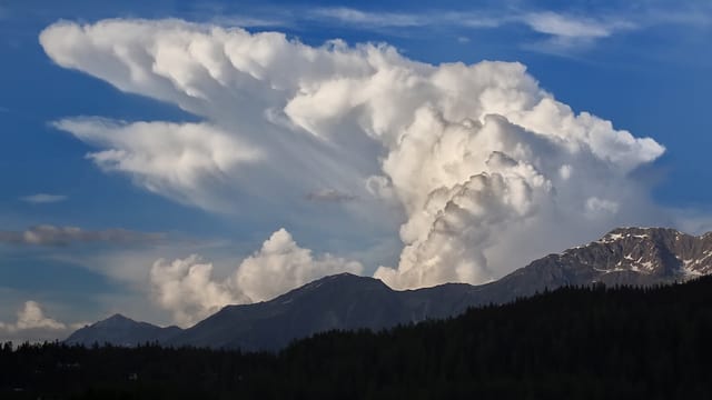 Riesige, weisse Gewitterwolke über den Alpen. Daneben blauer Himmel. Riesige, weisse Gewitterwolke über den Alpen. Daneben blauer Himmel.