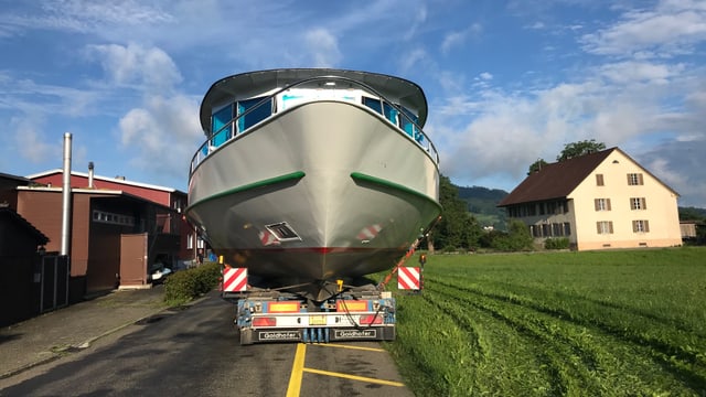 Das grosse Schiff wird angeliefert auf einem Lastwagen. Er fahrt auf einer kleinen, schmalen Strasse. Das grosse Schiff wird angeliefert auf einem Lastwagen. Er fahrt auf einer kleinen, schmalen Strasse.