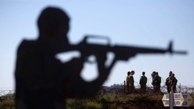 Umrisse eines Mannes mit Maschinengewehr im Anschlag, im Hintergrund eine Gruppe Soldaten. Umrisse eines Mannes mit Maschinengewehr im Anschlag, im Hintergrund eine Gruppe Soldaten.