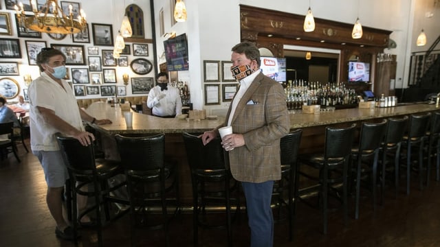 Zwei Männer mit Gesichtsmasken stehen an einer Bar Zwei Männer mit Gesichtsmasken stehen an einer Bar