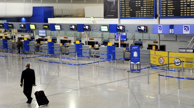 Ein Pilot mit Rollkoffer durchquert die leere Schalterhalle am Athener Flughafen. Ein Pilot mit Rollkoffer durchquert die leere Schalterhalle am Athener Flughafen.