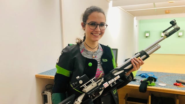 Purtret d'ina giuvna cun chavels stgirs, ella porta egliers e ri en la camera. Purtret d'ina giuvna cun chavels stgirs, ella porta egliers e ri en la camera.