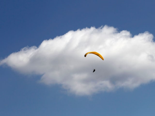 Blauer Himmel mit grosser weisser Wolke. Im Vordergrund ein Gleitschirmflieger mit gelbem Schirm. Blauer Himmel mit grosser weisser Wolke. Im Vordergrund ein Gleitschirmflieger mit gelbem Schirm.