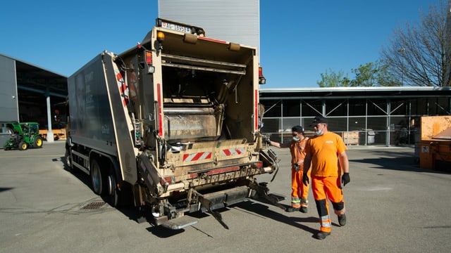 Der Arbeitstag zweier Müllmänner beginnt. Einer steht schon auf der Plattform der Kehrichtabfuhr und der andere springt drauf Der Arbeitstag zweier Müllmänner beginnt. Einer steht schon auf der Plattform der Kehrichtabfuhr und der andere springt drauf
