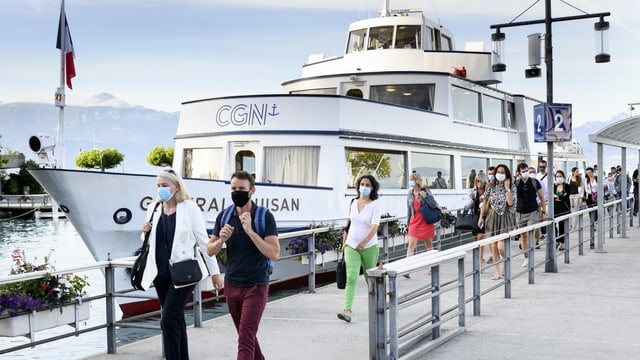 Menschen laufen auf dem Steg weg von einem Schiff. Alle tragen eine Maske über Nase, Mund und Kinn. Menschen laufen auf dem Steg weg von einem Schiff. Alle tragen eine Maske über Nase, Mund und Kinn.