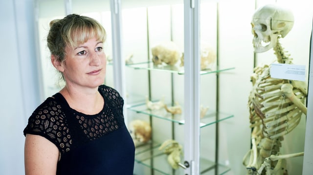 Eine Frau steht vor einer Vitrine mit Skeletten und Knochen. Eine Frau steht vor einer Vitrine mit Skeletten und Knochen.