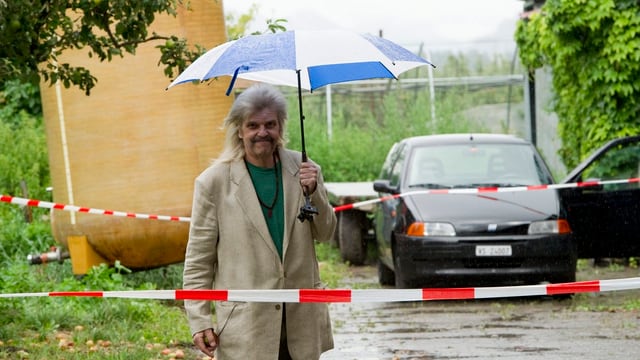 Mann mit Regenschirm auf einem Bauernhof.