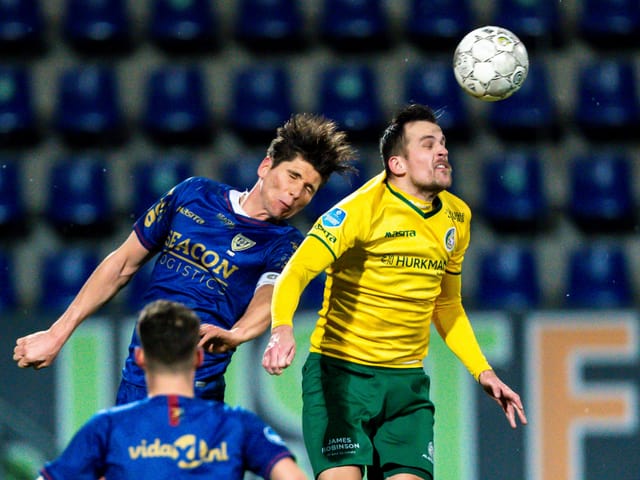 Zwei Spieler steigen mit geschlossenen Augen hoch zum Kopfballduell.