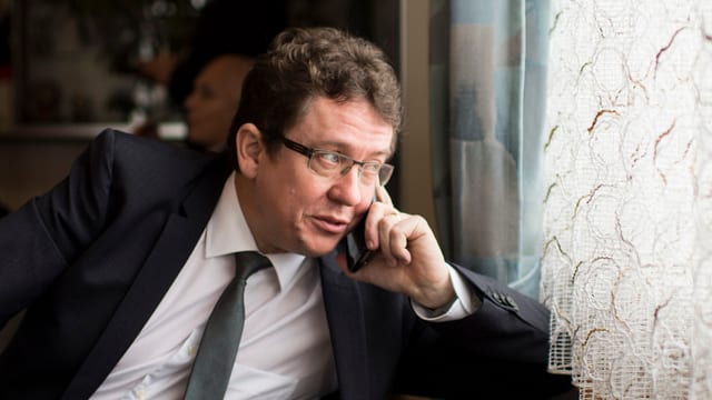 Ein Politiker im Anzug telefoniert am Fenster und blickt nach aussen Ein Politiker im Anzug telefoniert am Fenster und blickt nach aussen