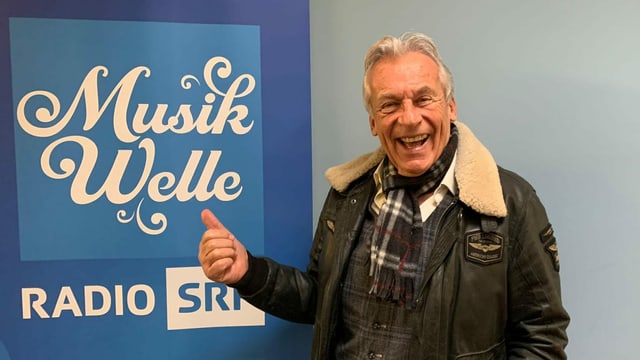 Pepe Lienhard steht vor Musikwelle Logo. Pepe Lienhard steht vor Musikwelle Logo.